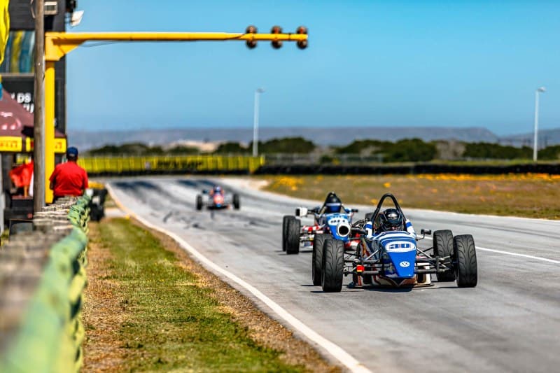 Open-wheel formula cars race past the start-finish gantry at Aldo Scribante Raceway, Port Elizabeth