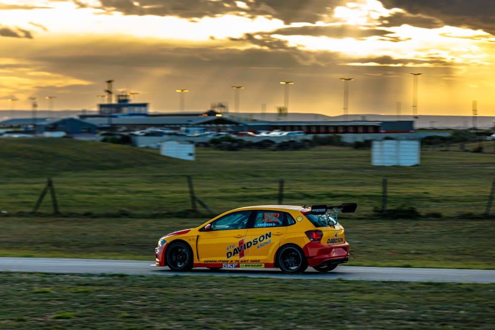 Yellow VW Polo touring car races at golden-hour dusk at Aldo Scribante Raceway, Port Elizabeth