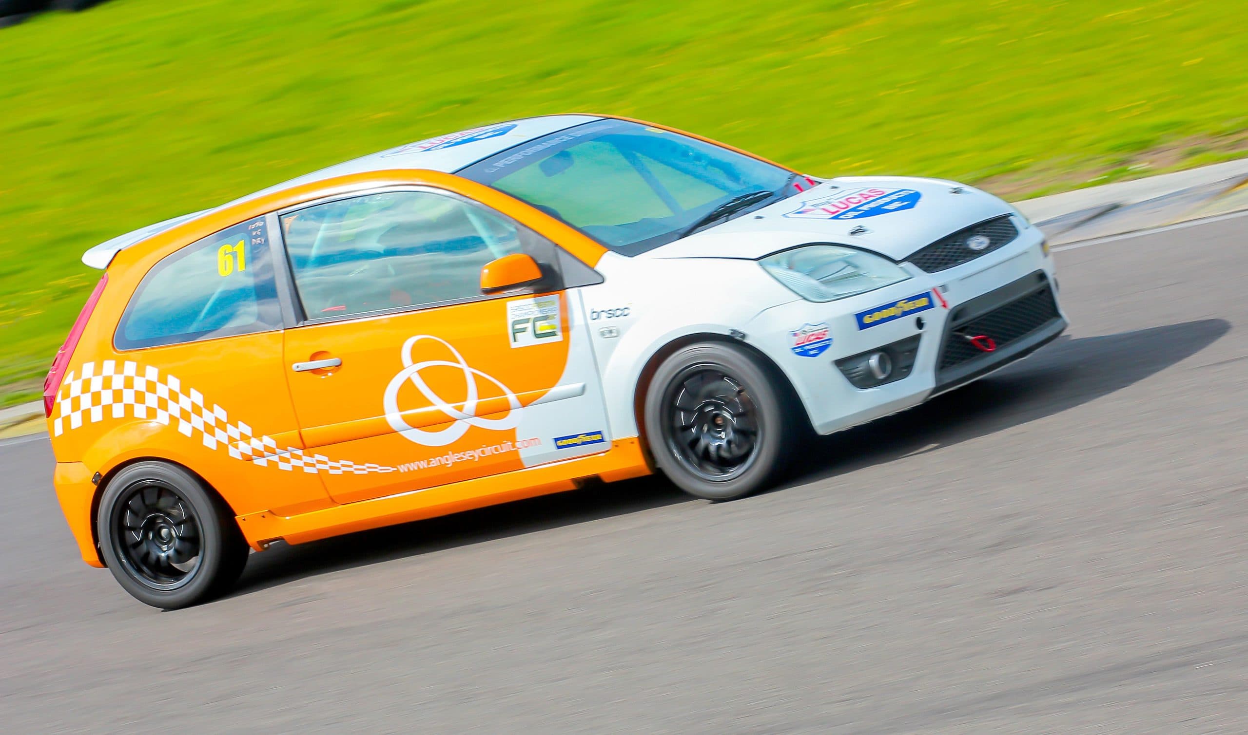 Orange and white Anglesey Circuit Ford Fiesta race car number 61 at speed on Trac Mon, Wales