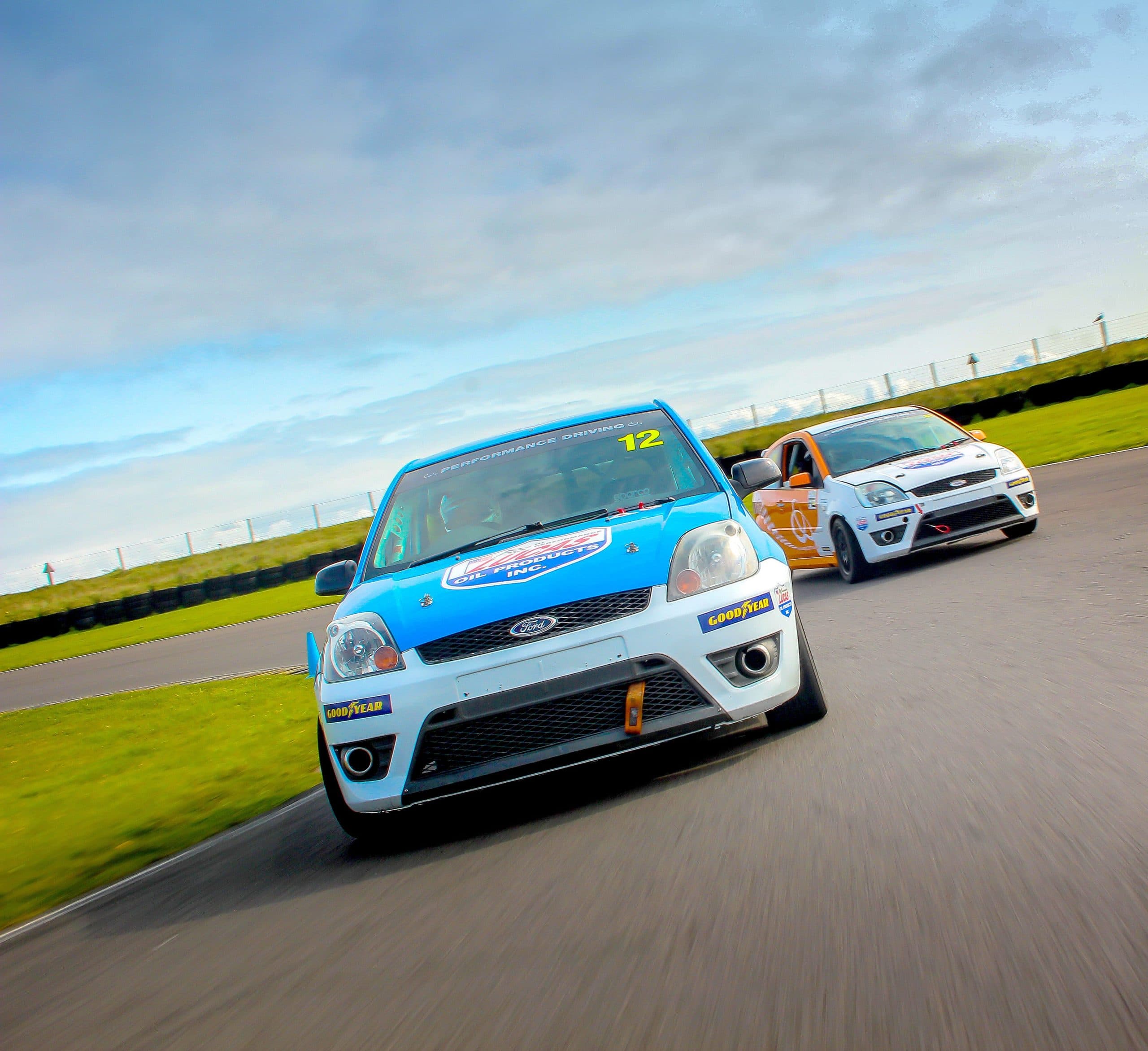 Two Ford Fiestas racing nose-to-tail on the circuit at Anglesey, Wales, under an overcast sky