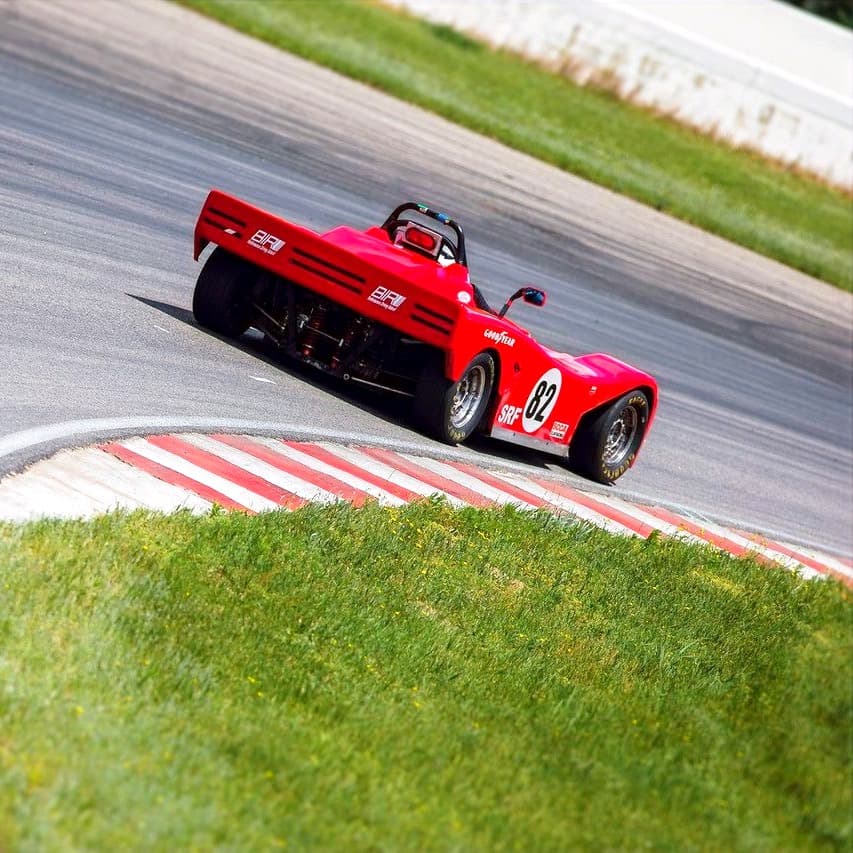 Vintage red BIR-liveried sports racer cornering on the road course at Brainerd International Raceway, Minnesota