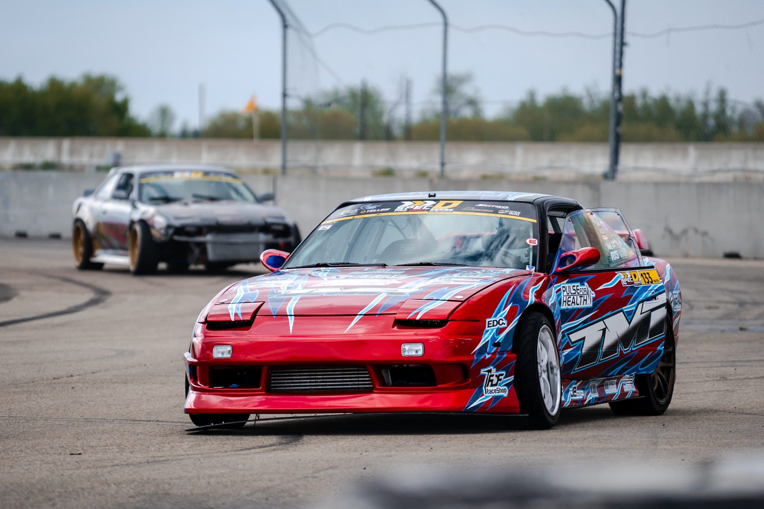 A red drift car chases a rival past the concrete wall at RAD Torque Raceway, Edmonton