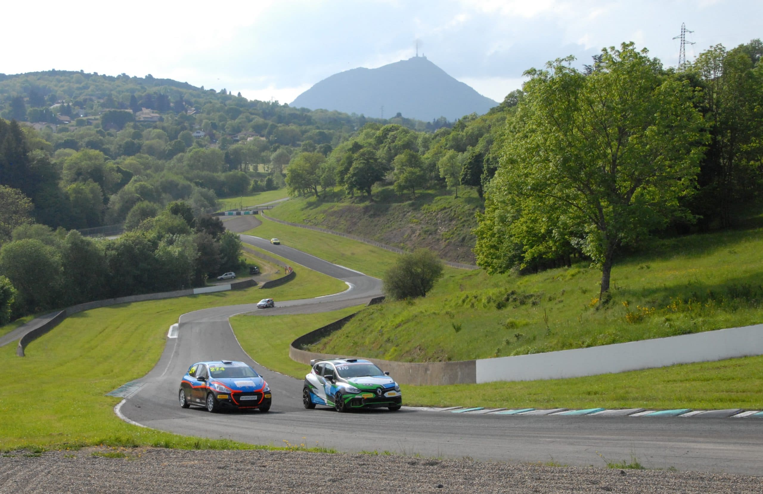 Two touring cars descend Charade hairpin curves with the Puy de Dome rising behind them