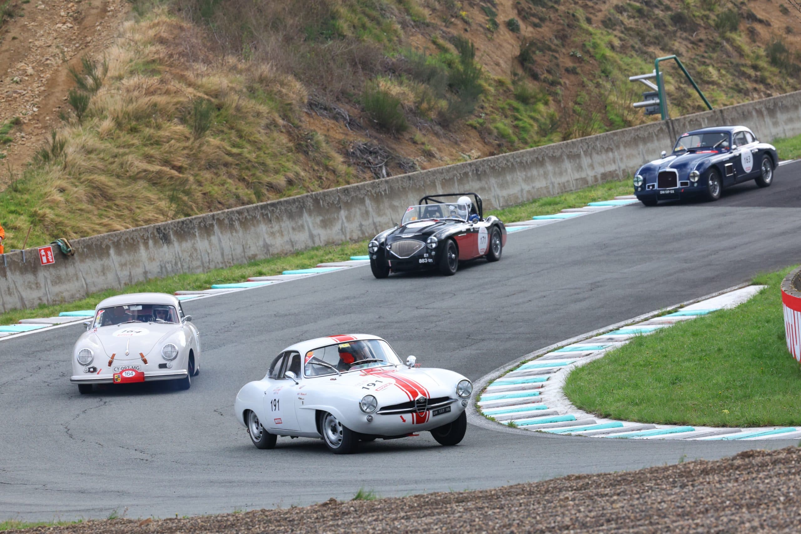 Vintage Porsche, Alfa Romeo, and Austin-Healey sports cars descend a hairpin during a historic race at Charade