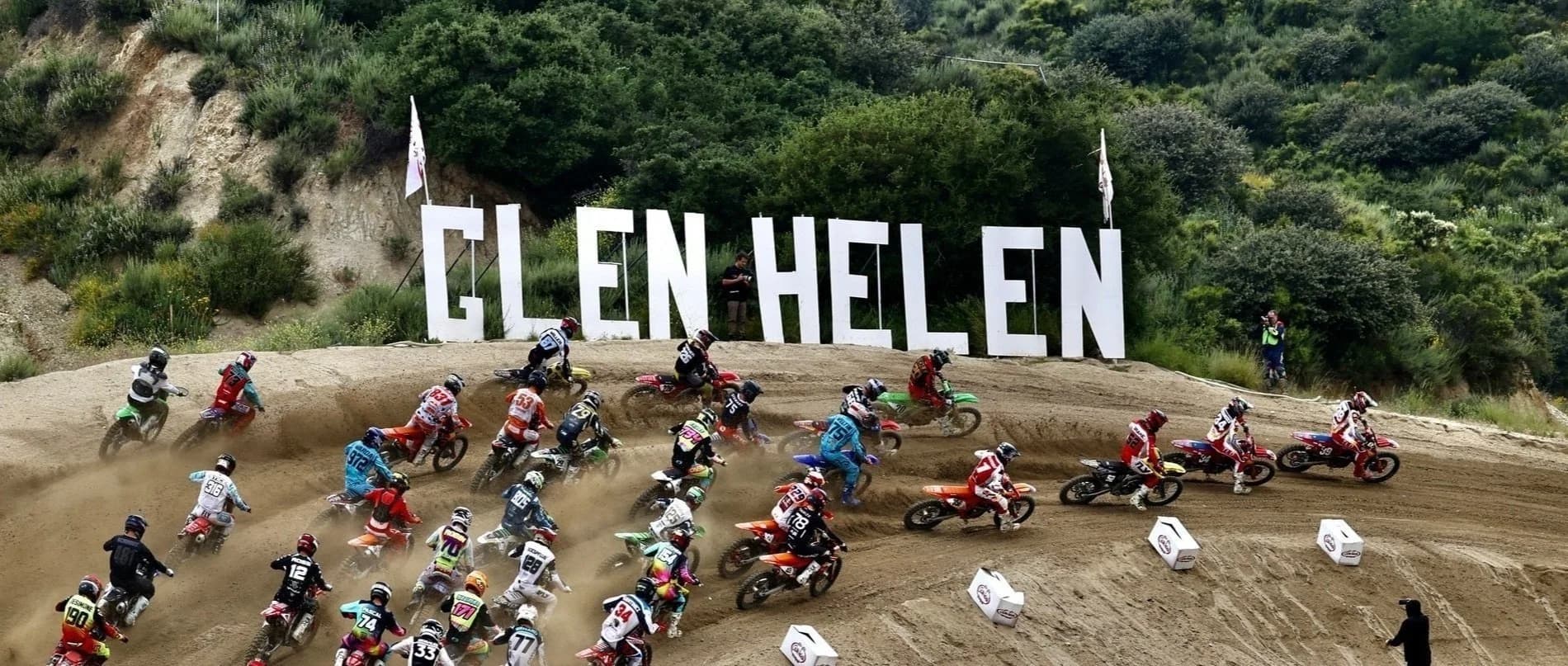 Large field of motocross riders launching off the start at Glen Helen Raceway, Rialto, California, with GLEN HELEN hillside sign in background
