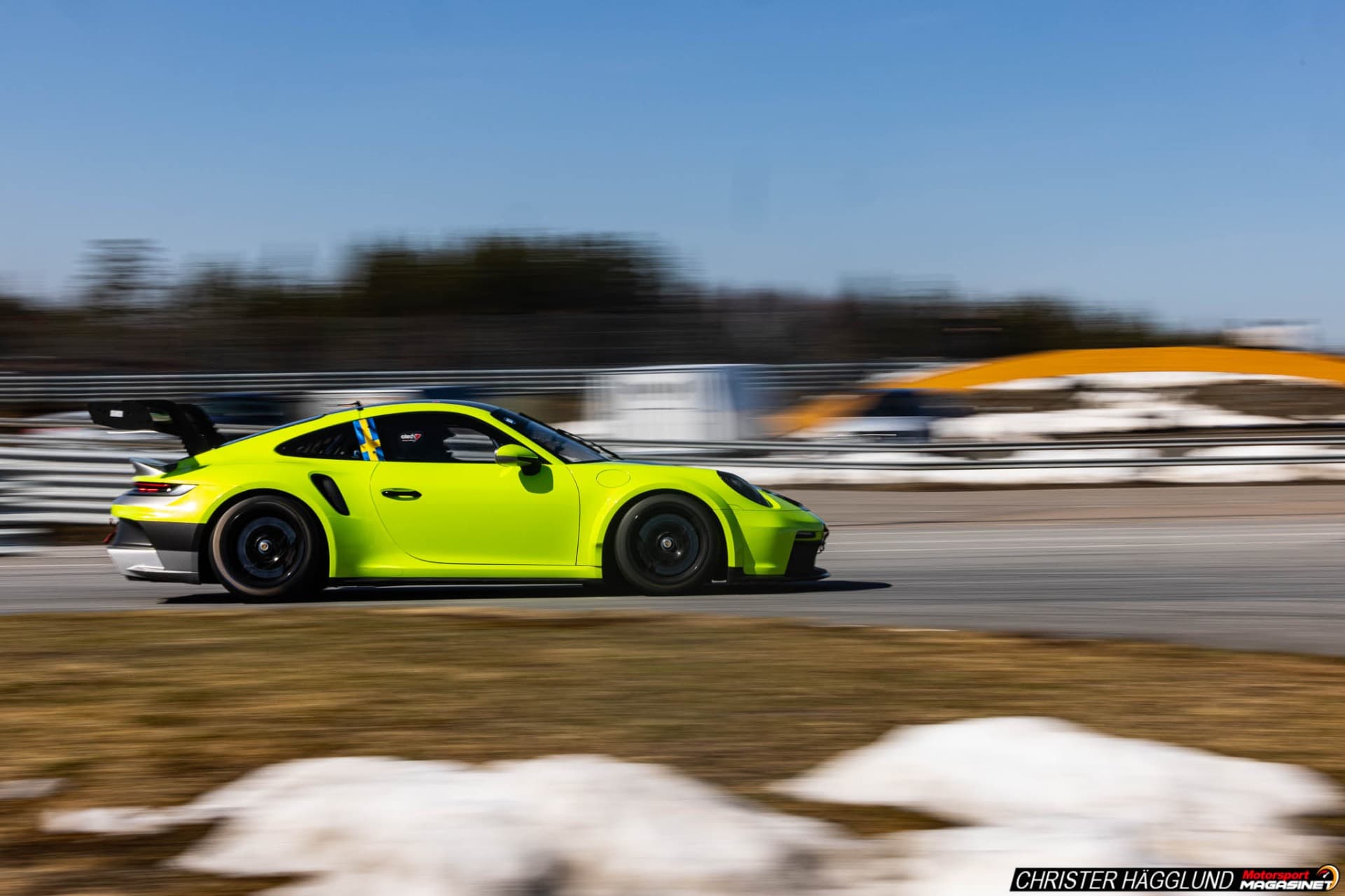 Neon yellow-green Porsche 911 GT3 RS cornering at speed on Mittsverigebanan road course, Härnösand, Sweden