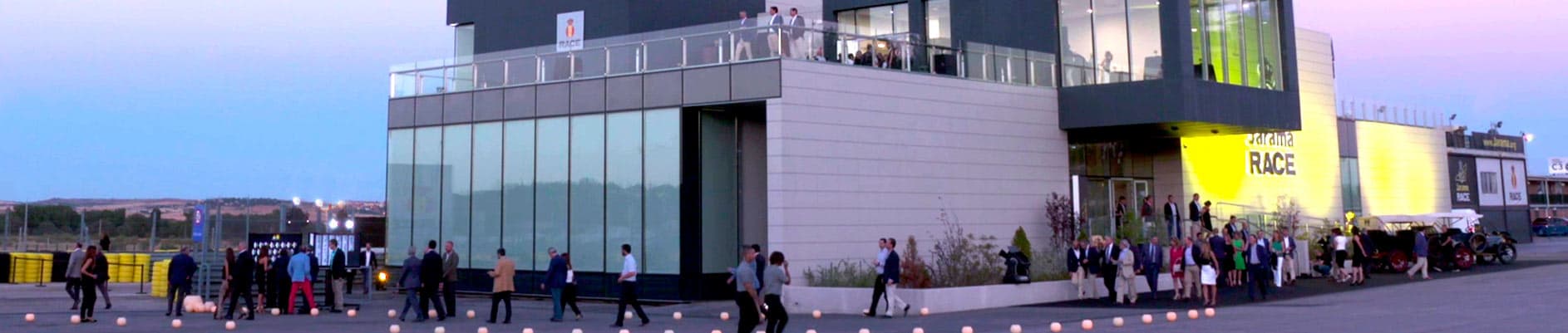 Outdoor evening event at the Jarama RACE pit building with guests gathered in the plaza, Madrid