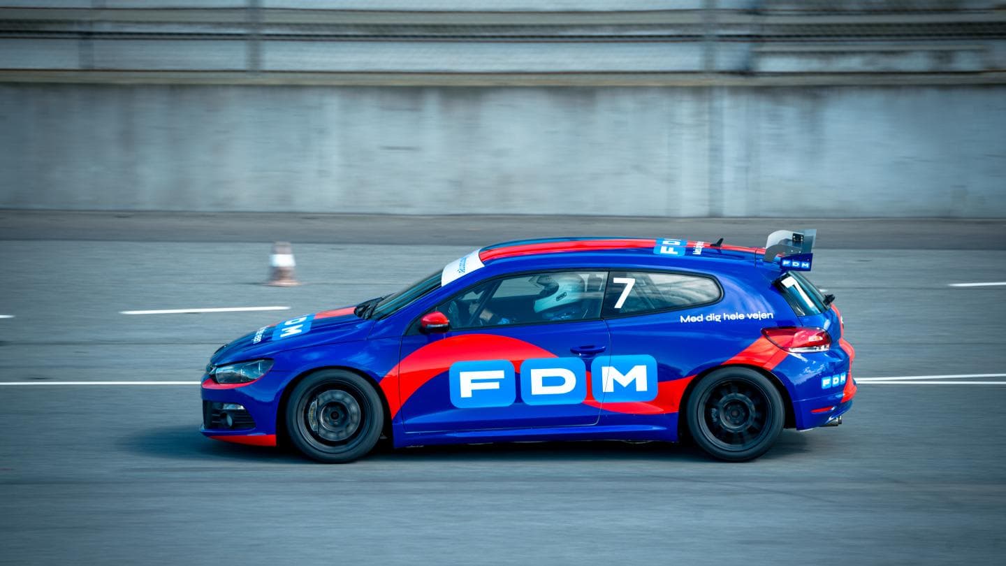 FDM-branded Volkswagen Scirocco race car in blue and red livery accelerating on track at Jyllandsringen