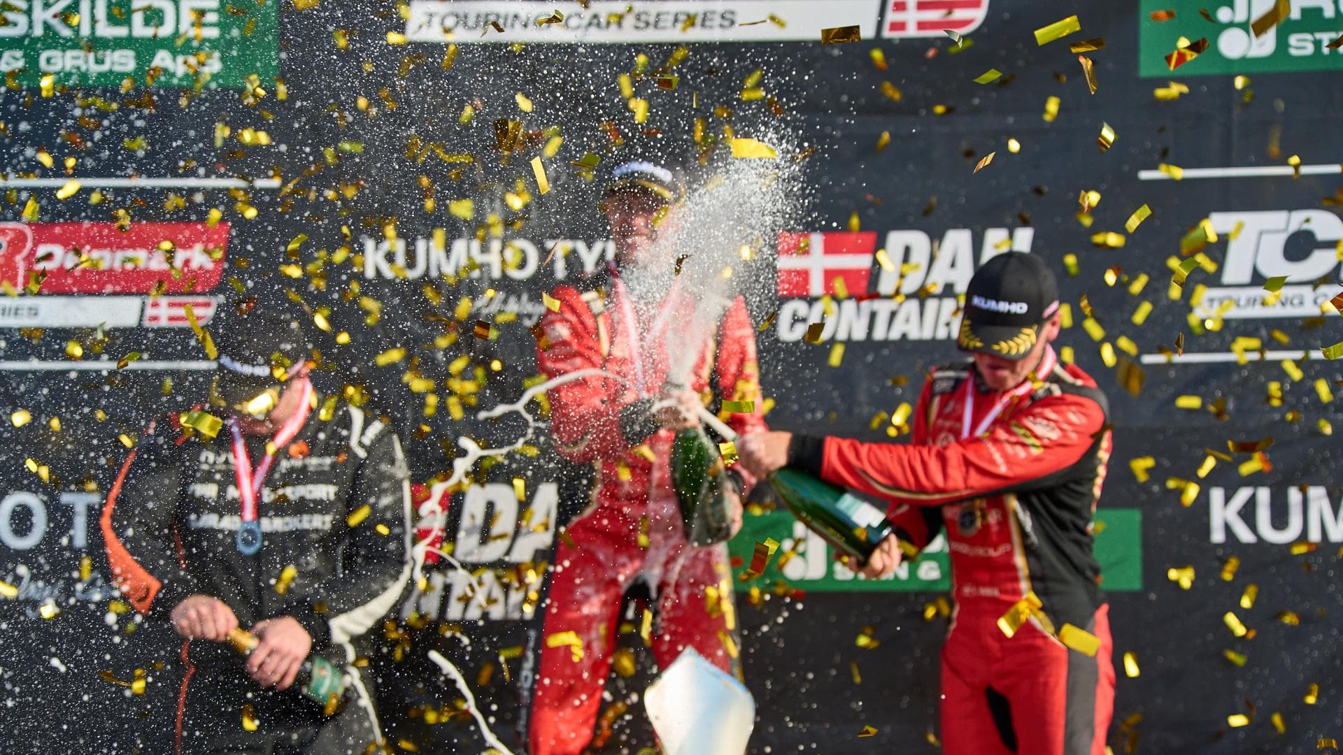 Race drivers in red suits spray champagne on the podium at FDM Jyllandsringen, Silkeborg, Denmark